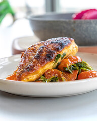Close-up photo of delicious cooked chicken breast served with spinach and cherry tomatoes. A clean, balanced, and healthy dinner