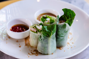 Four Vietnamese fresh spring rolls or gỏi cuốn on a plate with peanut sauce and hoisin chili sauce, ready to be enjoyed.