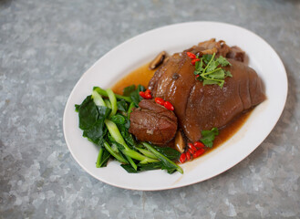 Stewed pork leg placed on a white plate on a metal background.
