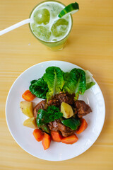 Overhead view of Filipino beef caldereta with lettuce and vegetables, served with iced cucumber juice on a bright wooden table.