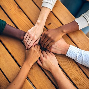 Hands joined together symbolizing unity diversity cooperation and teamwork on a wooden table