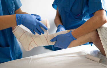 Doctors applying bandage on patient's injured foot in hospital room