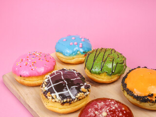 Colorful assorted donuts with vibrant icing and toppings on a wooden tray over a pink background