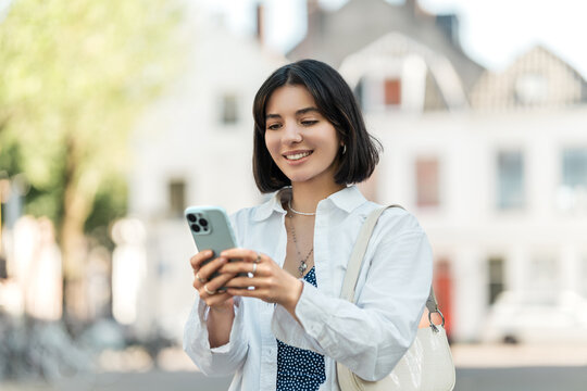 Waiting for directions to load, a stylish young woman of mixed heritage scrolls her phone against a charming European backdrop