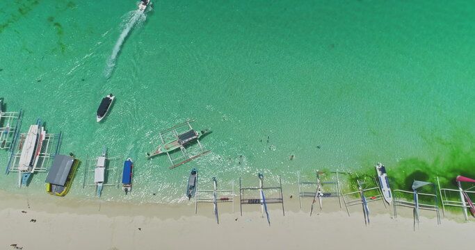 Aerial view of White Beach in Boracay, Philippines, featuring iconic paraw sailboats in turquoise waters, with a speedboat enhancing the vibrant tropical scene
