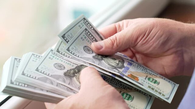 Counting Cash at a Window During the Day With Natural Light Illuminating the Bills Close Up. A person counts a stack of cash, segregating various bills