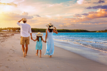 A beautiful family on summer holidays walks on a tropical beach during golden sunset time as a...