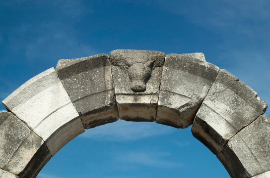 Ancient stone arch and keystone with bull head on entrance to the amphitheatre in blue sky