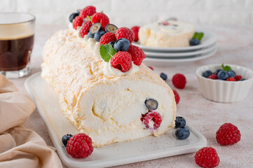 Meringue Pavlova roll cake with cream and fresh berries on top on a ceramic board on a concrete background. Copy space.
