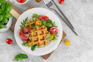 Spinach waffles with tomatoes, arugula and prosciutto on a white plate with a cup of coffee....