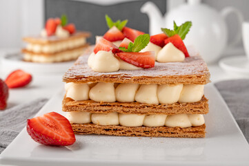 French dessert millefeuille with vanilla cream and fresh strawberries on a white plate on a white wooden background.