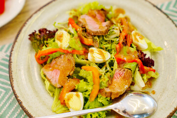 A plate of meat salad made from lettuce, quail egg, vegetables and steak.