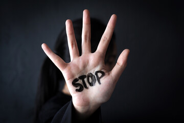 Young Woman With Word STOP Written On Her Palm Against Dark Background