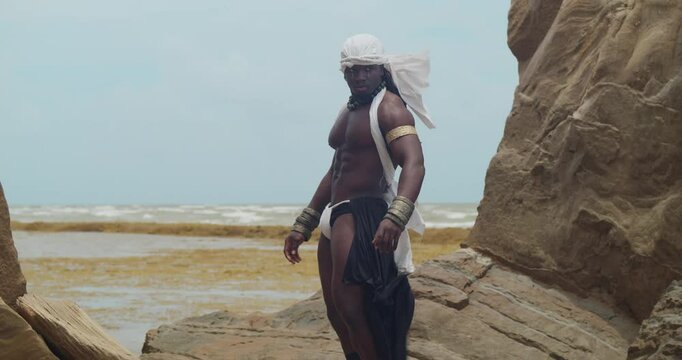 A male cosplayer, his dark skin and muscles prominent on the beach.