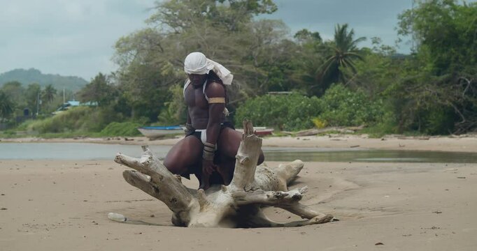 Dark skin and muscles on a male cosplayer at the beach on a log