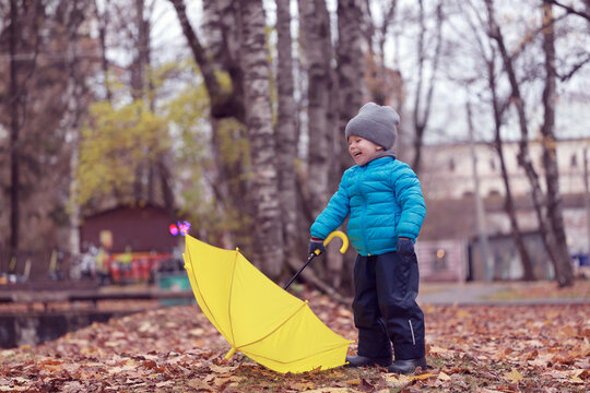 A boy with an umbrella and autumn leaves falling in the park on a walk