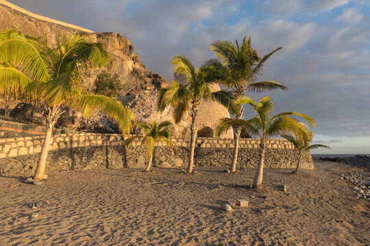 Picturesque empty golden sand beach with palm trees and stone wall in Playa de San Juan. Playa de San Juan is a small fishing village on the south west of Tenerife island. Golden hour light