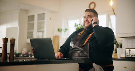 Phone call, chef and man with smile, kitchen and communication with supplier for ingredients order. Talking, cook and person with mobile for chat with contact, house and planning for menu with laptop