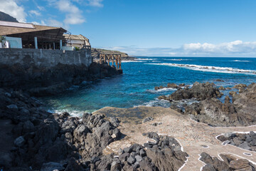 Old fish factory building at center of Garachico old town with sea pools and lava rocks at Tenerife canary island, Spain. Blue sky white clouds background