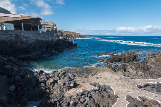 Old fish factory building at center of Garachico old town with sea pools and lava rocks at Tenerife canary island, Spain. Blue sky white clouds background