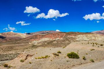 A scenic road stretches through a mountain landscape under a clear blue sky. The yellow lines guide the way through the impressive Argentine mountains.