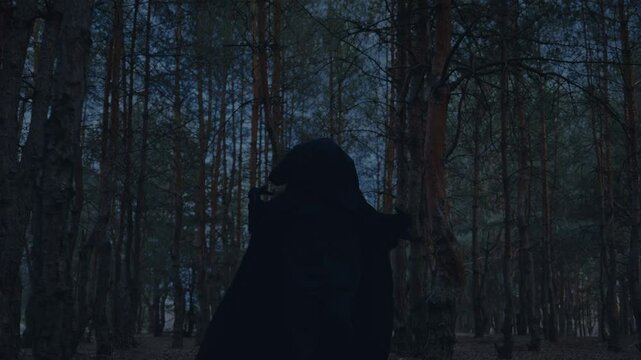 Gothic unrecognizable person evil paranormal character running in night dark dusk forest. Angel of death, monster nightmare scares is chasing victim. Fantasy evil man in black hood cape. hide face