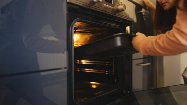 Smiling mom and daughter putting tray with cookies in oven, home baking time