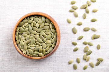 Pepitas, hulled pumpkin seeds, in a wooden bowl, on linen. Raw, dried squash seeds, fruits of Cucurbita, light green after the husk is removed, and used as snack, garnish or as an ingredient. Photo