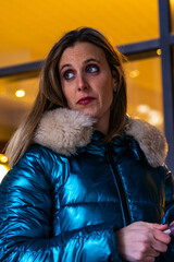 Woman wearing blue puffer jacket with fur collar looking away