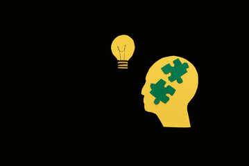 yellow Silhouette of a head with puzzle pieces and a lightbulb on Black Background, concept of...