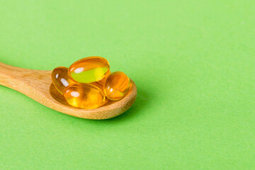 Vitamin omega capsules in a spoon on a colored background. Pills served as a healthy meal. Red soft...
