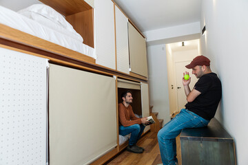 Modern hostel with cozy minimalist dorms, wooden capsule beds, and peaceful courtyard. Men chatting...