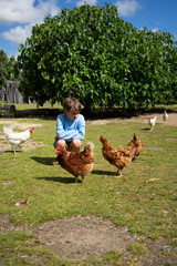 Young boy crouching and interacting with chickens in a farm setting
