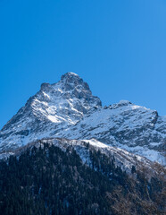 Karachay-Cherkessia. Dombay 2025. Majestic snow-covered mountain peak stands tall against clear blue sky, showcasing rugged beauty of winter landscape. Nature concept for design.