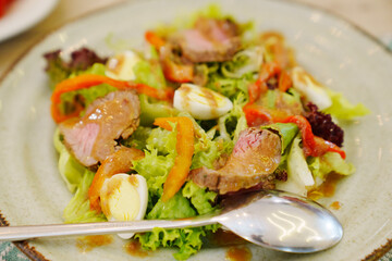 A plate of meat salad made from lettuce, quail egg, vegetables and steak.