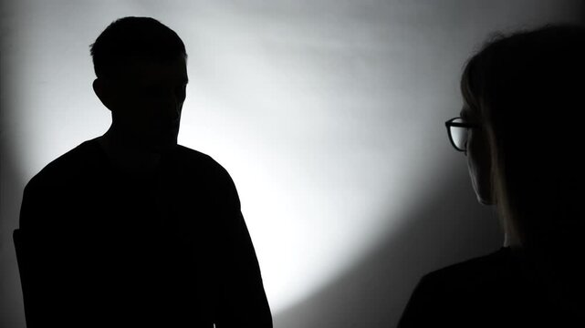 Silhouette of hidden man in dark room talking to woman. Interview concept. Anonymous person.