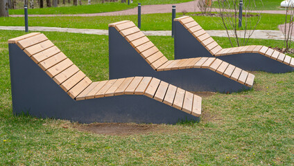 Empty wooden deck chairs or sun beds in city park.