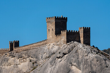 Fortress wall of  Genoese fortress stands atop rocky from Cape Alchak, surrounded by rugged terrain and sparse vegetation, showcasing ancient architecture against a natural backdrop. Sudak, Crimea