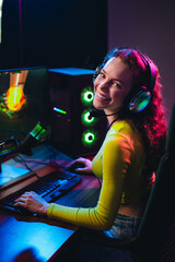 Plakat Young woman gaming with headset and colorful neon lights at night in modern home setup enjoying online streaming