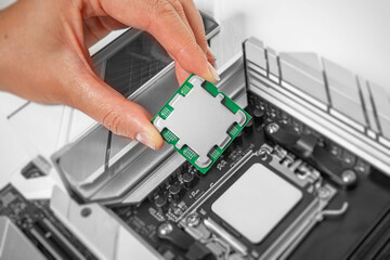 A person is carefully holding a computer processor above a motherboard socket, preparing to install it.