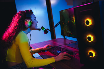 Positive enthusiastic female gamer streaming video games at home with vibrant neon lighting in a...