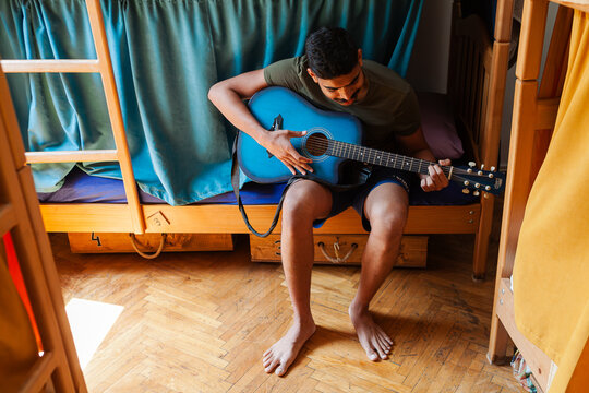 Colourful art hostel in old town with budget-friendly dorms, painted walls, shared kitchen, urban views. Diverse traveler plays guitar and relaxes
