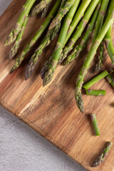 Asparagus stems arranged on wooden cutting board, asparagus fresh on gray kitchen surface,...