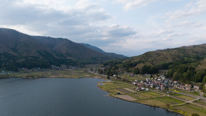 Aerial view by drone Tranquil village nestled between lush green mountains and a calm lake, showcasing the serene beauty of rural life nature of Matsumoto Japan.