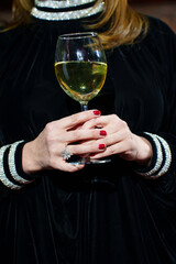 A glass of white wine or champagne in a woman's hand.