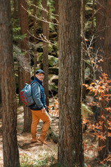 Smiling man with glasses and backpack hiking in a beautiful pine forest. Standing on mossy rocks,...