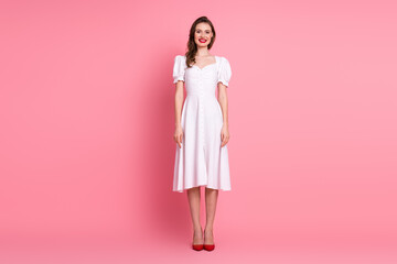 Smiling young woman wearing a white dress posing confidently against a pink background, showcasing charm and elegance