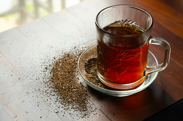 Cup of hot black tea and tea leaf on the wooden table.