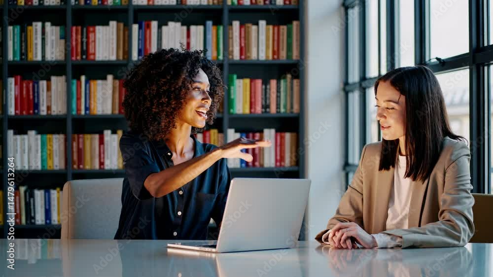 Poster two professionals in a library setting, smiling and working on a laptop. the video captures a side a