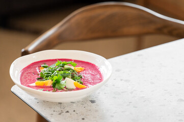 A bowl of vibrant beetroot soup garnished with fresh greens and slices of boiled egg, placed on a...